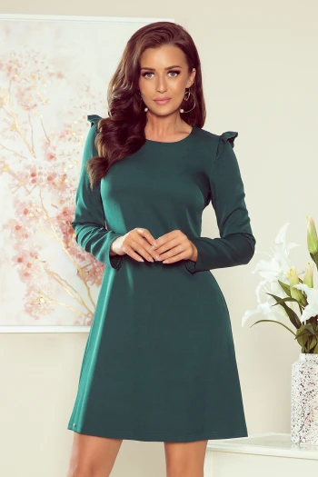 Modelka prezentuje elegancką sukienkę z długim rękawem, która doskonale podkreśla sylwetkę. Ta zielona sukienka to idealny wybór na każdą okazję, łącząc klasyczny styl z nowoczesnym akcentem.