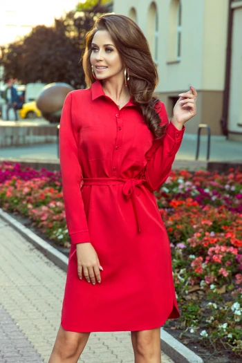 Modelka prezentuje elegancką czerwoną sukienkę koszulową, która doskonale podkreśla kobiecą sylwetkę. Ta sukienka koszulowa z paskiem to idealny wybór na każdą okazję, łącząc styl z wygodą.
