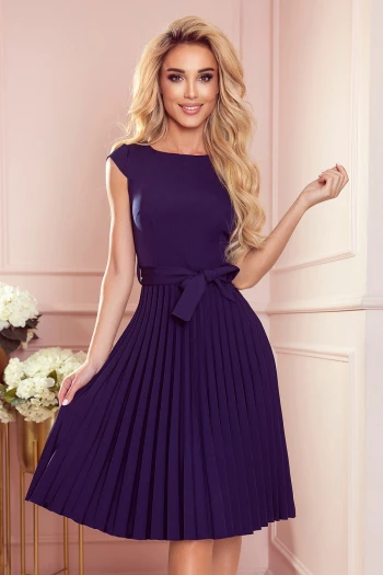 Kobieta na zdjęciu prezentuje elegancką sukienkę plisowaną, która podkreśla jej sylwetkę i dodaje klasycznego uroku. Sukienka plisowana z wiązaniem w pasie idealnie sprawdzi się na wyjątkowe okazje, łącząc styl i wygodę.