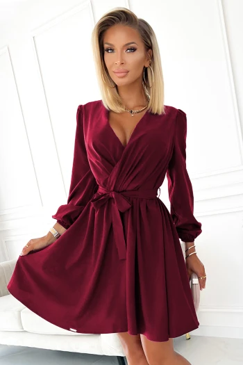 Kobieta na zdjęciu prezentuje elegancką sukienkę kopertową w głębokim odcieniu czerwieni, która podkreśla jej sylwetkę i dodaje klasy. Sukienka kopertowa z wiązaniem w talii to idealny wybór na wieczorne wyjścia, łącząc styl z wygodą.