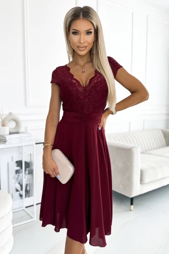 Modelka prezentuje elegancką sukienkę z koronkowym dekoltem w kolorze bordowym, która idealnie podkreśla sylwetkę. Ta bordowa sukienka z koronką to doskonały wybór na wyjątkowe okazje, łączący klasykę z nowoczesnym stylem.