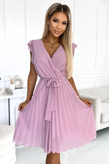 Kobieta na zdjęciu prezentuje elegancką sukienkę plisowaną w kolorze liliowym, która idealnie podkreśla jej sylwetkę. Sukienka plisowana z wiązaniem w talii dodaje stylizacji lekkości i kobiecego uroku.