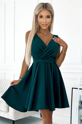 Kobieta na zdjęciu prezentuje elegancką sukienkę koktajlową z głębokim dekoltem, która podkreśla jej sylwetkę. Sukienka koktajlowa w kolorze butelkowej zieleni dodaje szyku i idealnie nadaje się na wyjątkowe okazje.