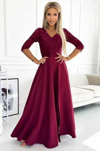 Modelka prezentuje elegancką suknię wieczorową w głębokim odcieniu czerwieni, która doskonale podkreśla sylwetkę i dodaje klasy każdej stylizacji. Suknia wieczorowa wyróżnia się koronkowym wykończeniem górnej części oraz zwiewnym, rozkloszowanym dołem, idealnym na wyjątkowe okazje.