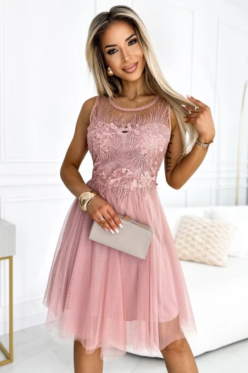Kobieta na zdjęciu prezentuje elegancką sukienkę wieczorową w odcieniu pudrowego różu, która zachwyca delikatnym tiulowym wykończeniem i misternymi haftami. Ta sukienka wieczorowa idealnie podkreśla sylwetkę, dodając szyku i klasy każdej stylizacji.