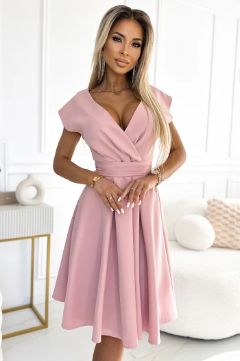 Modelka prezentuje elegancką sukienkę midi w kolorze pudrowego różu, która podkreśla kobiecą sylwetkę dzięki dopasowanemu krojowi i delikatnemu dekoltowi. Ta różowa sukienka midi to idealny wybór na wyjątkowe okazje, łącząc w sobie klasykę z nowoczesnym stylem.