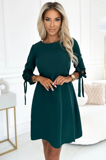 Modelka prezentuje elegancką sukienkę z wiązaniami na rękawach, która idealnie podkreśla sylwetkę. Ta stylowa sukienka to doskonały wybór na każdą okazję, łącząc klasykę z nowoczesnym akcentem.