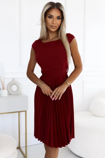 Modelka prezentuje elegancką sukienkę midi w głębokim odcieniu czerwieni, która podkreśla jej sylwetkę i dodaje klasy. Sukienka midi z plisowanym dołem doskonale sprawdzi się na wyjątkowe okazje, łącząc styl z wygodą.
