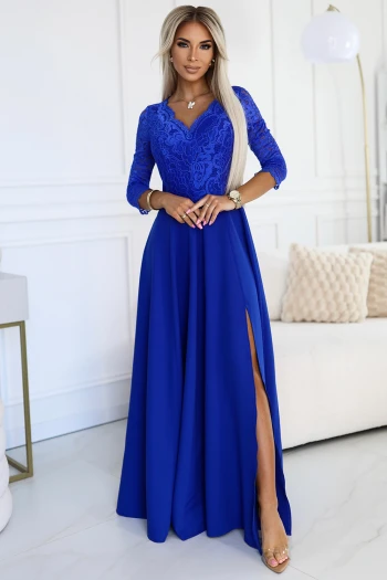 Kobieta na zdjęciu prezentuje elegancką suknię wieczorową w głębokim odcieniu niebieskiego, która podkreśla jej sylwetkę i dodaje szyku. Suknia wieczorowa wyróżnia się koronkowym wykończeniem na górze oraz efektownym rozcięciem, które dodaje jej zmysłowego charakteru.