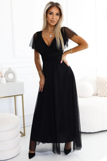 Modelka prezentuje elegancką sukienkę wieczorową, która zachwyca klasycznym krojem i delikatnym tiulowym wykończeniem. Ta czarna sukienka wieczorowa podkreśla sylwetkę, dodając jej szyku i wyjątkowego uroku.