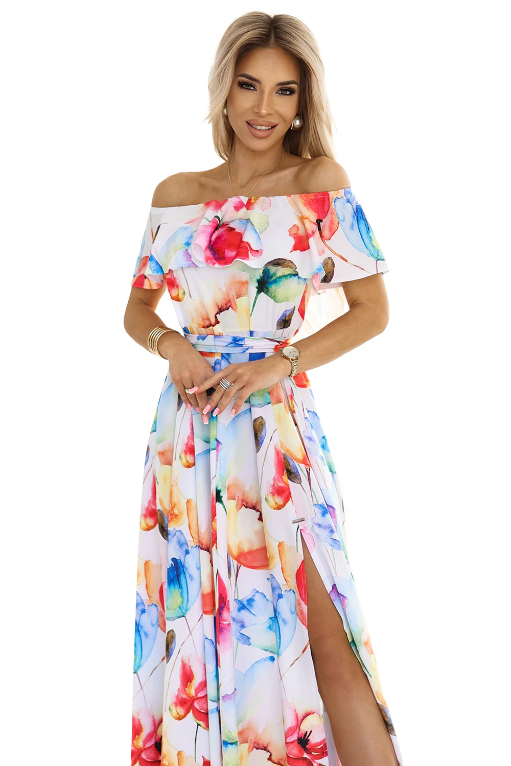 Modelka prezentuje elegancką sukienkę w kwiaty, która zachwyca żywymi kolorami i subtelnym krojem odkrywającym ramiona. Ta kwiecista sukienka to idealny wybór na letnie przyjęcia, podkreślający kobiecość i styl.