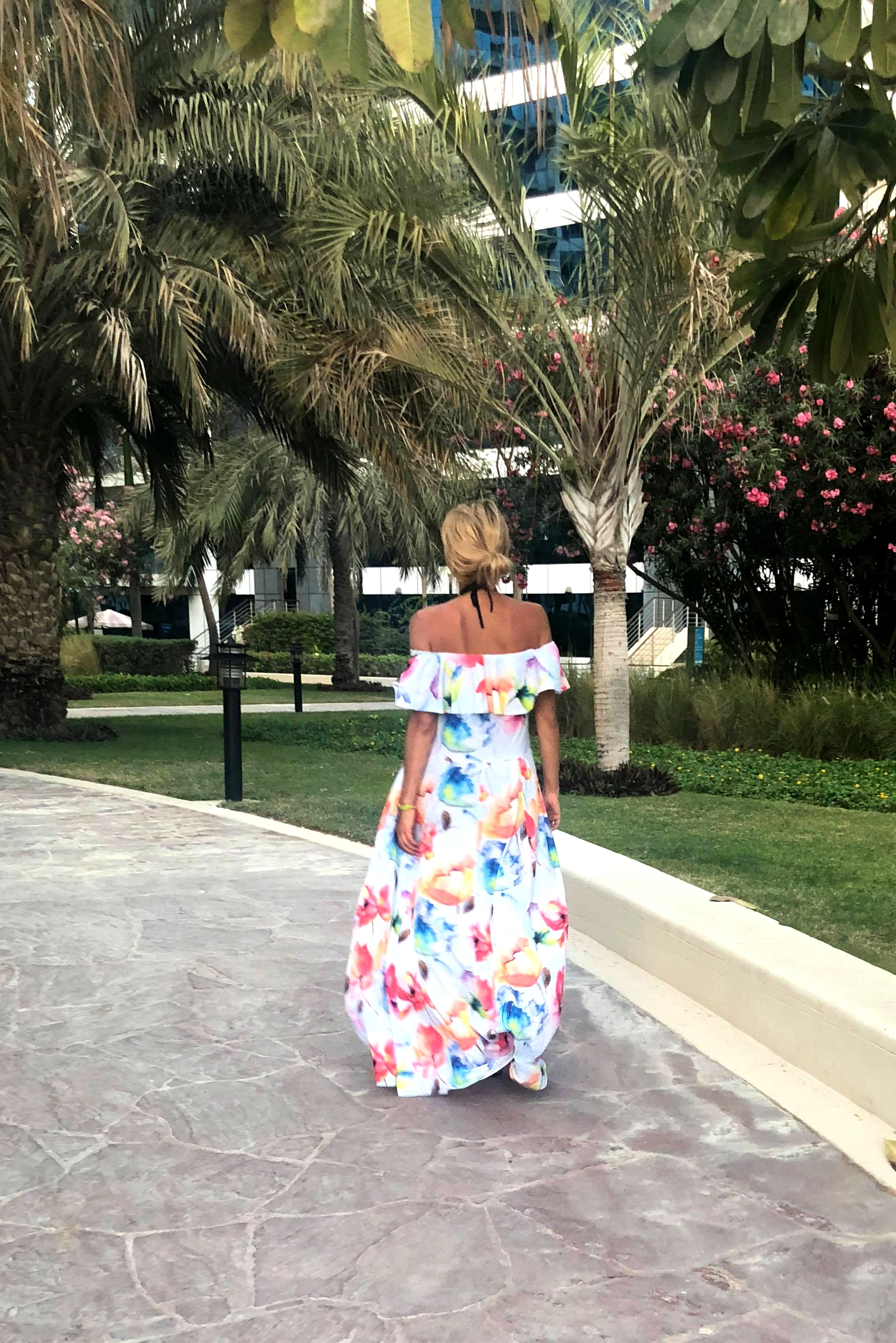 Modelka prezentuje elegancką sukienkę maxi w kwiaty, która idealnie podkreśla letni styl i swobodę. Sukienka maxi w kwiaty dodaje uroku i lekkości, doskonale komponując się z otoczeniem pełnym zieleni.