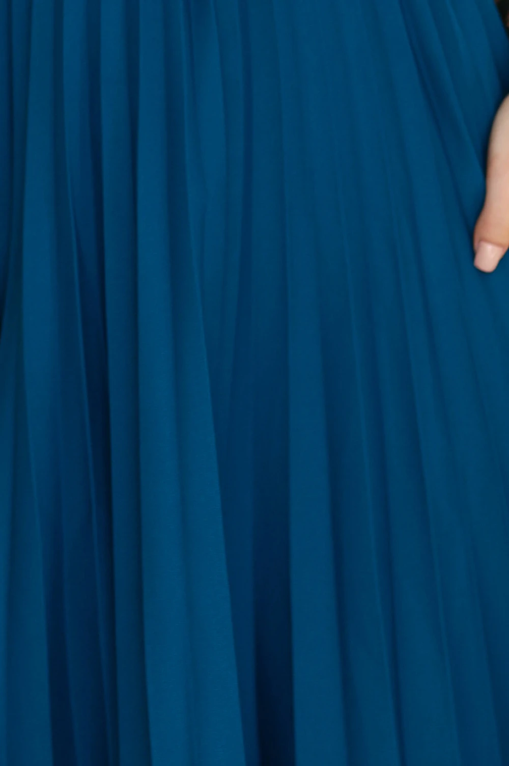 Modelka prezentuje elegancką, plisowaną spódnicę w głębokim odcieniu niebieskiego, która doskonale podkreśla sylwetkę. Ta niebieska spódnica z plisami to idealny wybór na każdą okazję, dodając stylu i klasy każdej stylizacji.