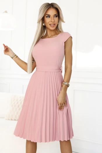 Modelka prezentuje elegancką sukienkę plisowaną w delikatnym odcieniu różu, która idealnie podkreśla kobiecą sylwetkę. Ta różowa sukienka plisowana to doskonały wybór na wyjątkowe okazje, łącząc klasykę z nowoczesnym stylem.