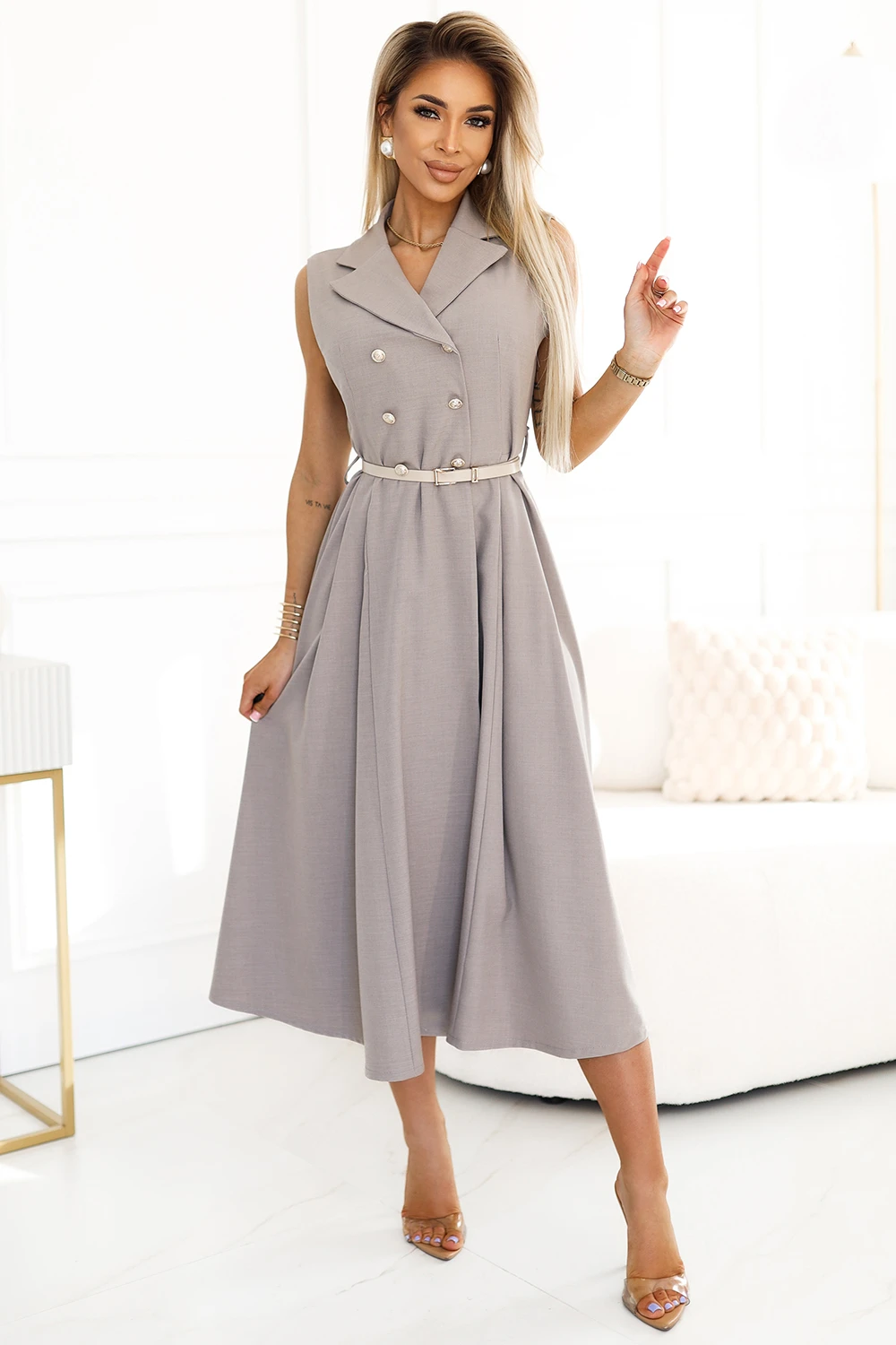 Modelka prezentuje elegancką sukienkę midi z podwójnym rzędem guzików, która idealnie łączy klasykę z nowoczesnym stylem. Sukienka midi podkreśla sylwetkę dzięki subtelnemu paskowi w talii, dodając całości wyrafinowanego charakteru.