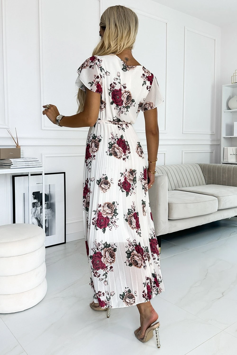 Modelka prezentuje elegancką sukienkę w kwiaty, która idealnie podkreśla kobiecą sylwetkę. Ta kwiecista sukienka to doskonały wybór na letnie przyjęcia, łącząc w sobie styl i wygodę.