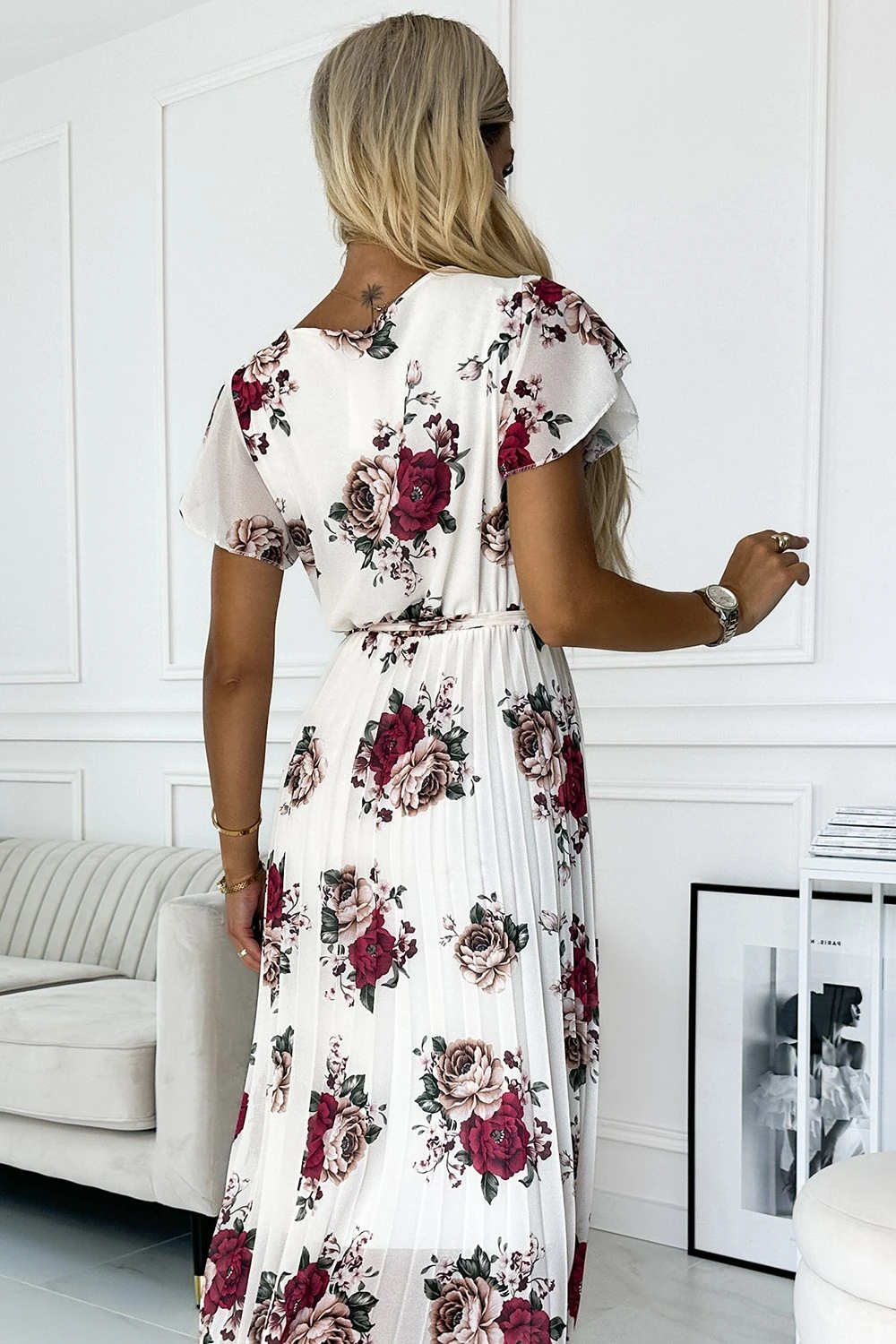 Modelka prezentuje elegancką sukienkę w kwiaty, która zachwyca swoim romantycznym wzorem i delikatnym materiałem. Sukienka w kwiaty idealnie podkreśla kobiecą sylwetkę, dodając stylizacji lekkości i wdzięku.