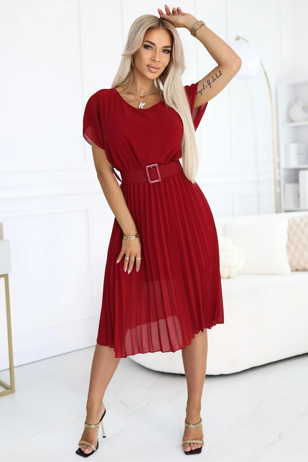 Kobieta na zdjęciu prezentuje elegancką sukienkę midi w kolorze głębokiej czerwieni, która idealnie podkreśla jej sylwetkę. Sukienka midi z paskiem dodaje stylizacji wyrafinowanego charakteru, idealnego na wyjątkowe okazje.