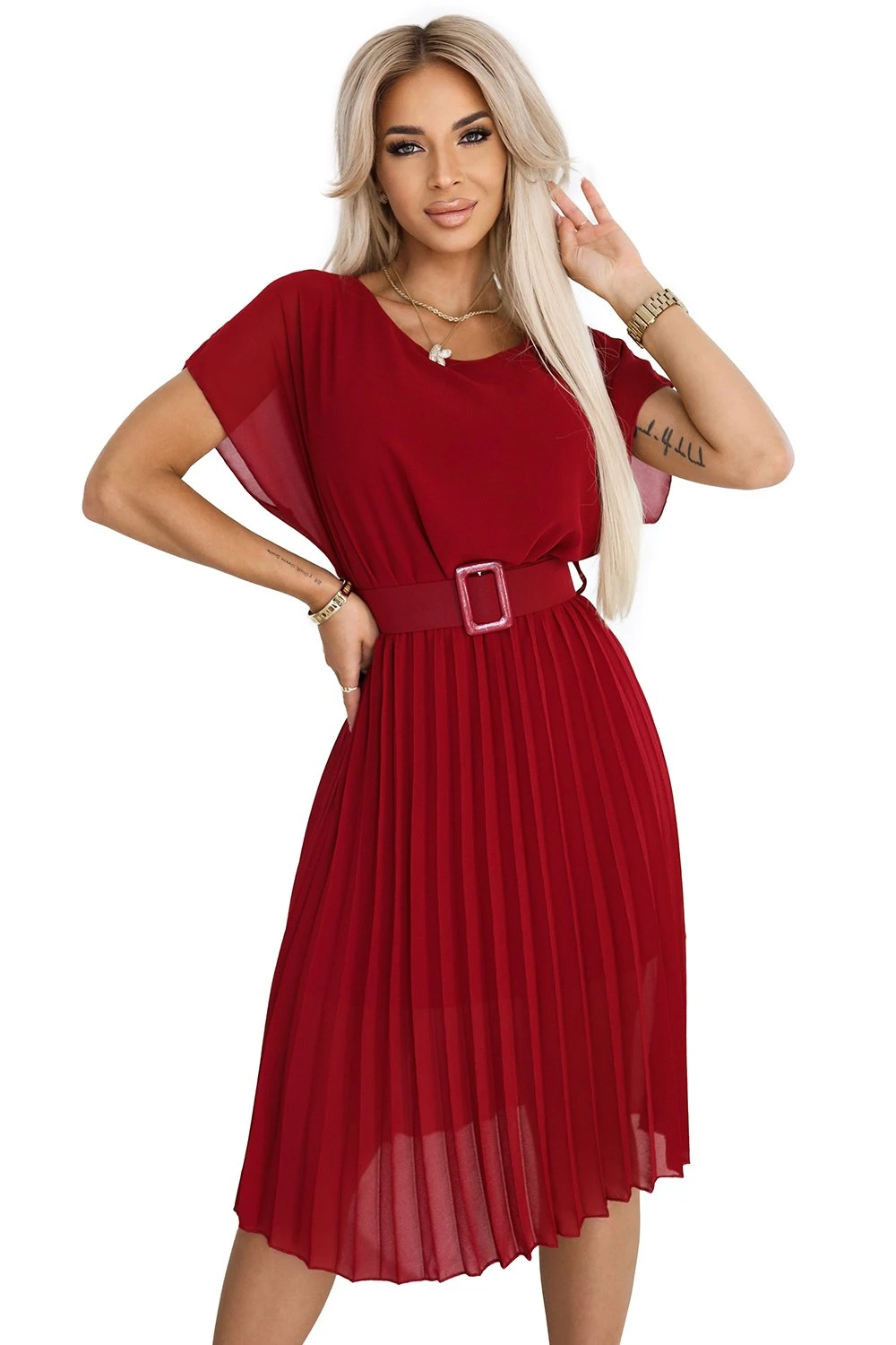 Modelka prezentuje elegancką sukienkę plisowaną w głębokim odcieniu czerwieni, która idealnie podkreśla sylwetkę. Sukienka plisowana z paskiem dodaje stylizacji szyku i nowoczesności, doskonale sprawdzając się na różne okazje.