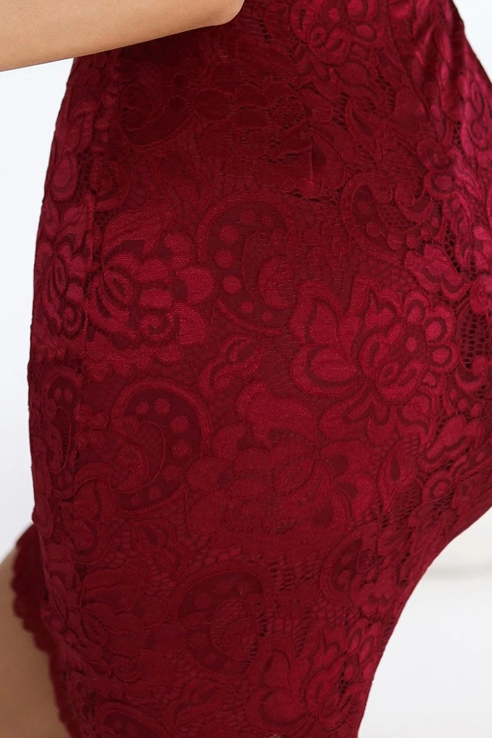 Modelka prezentuje elegancką sukienkę koronkową w głębokim odcieniu czerwieni, która idealnie podkreśla kobiece kształty. Sukienka koronkowa wyróżnia się misternym wzorem, dodającym jej wyjątkowego uroku i klasy.