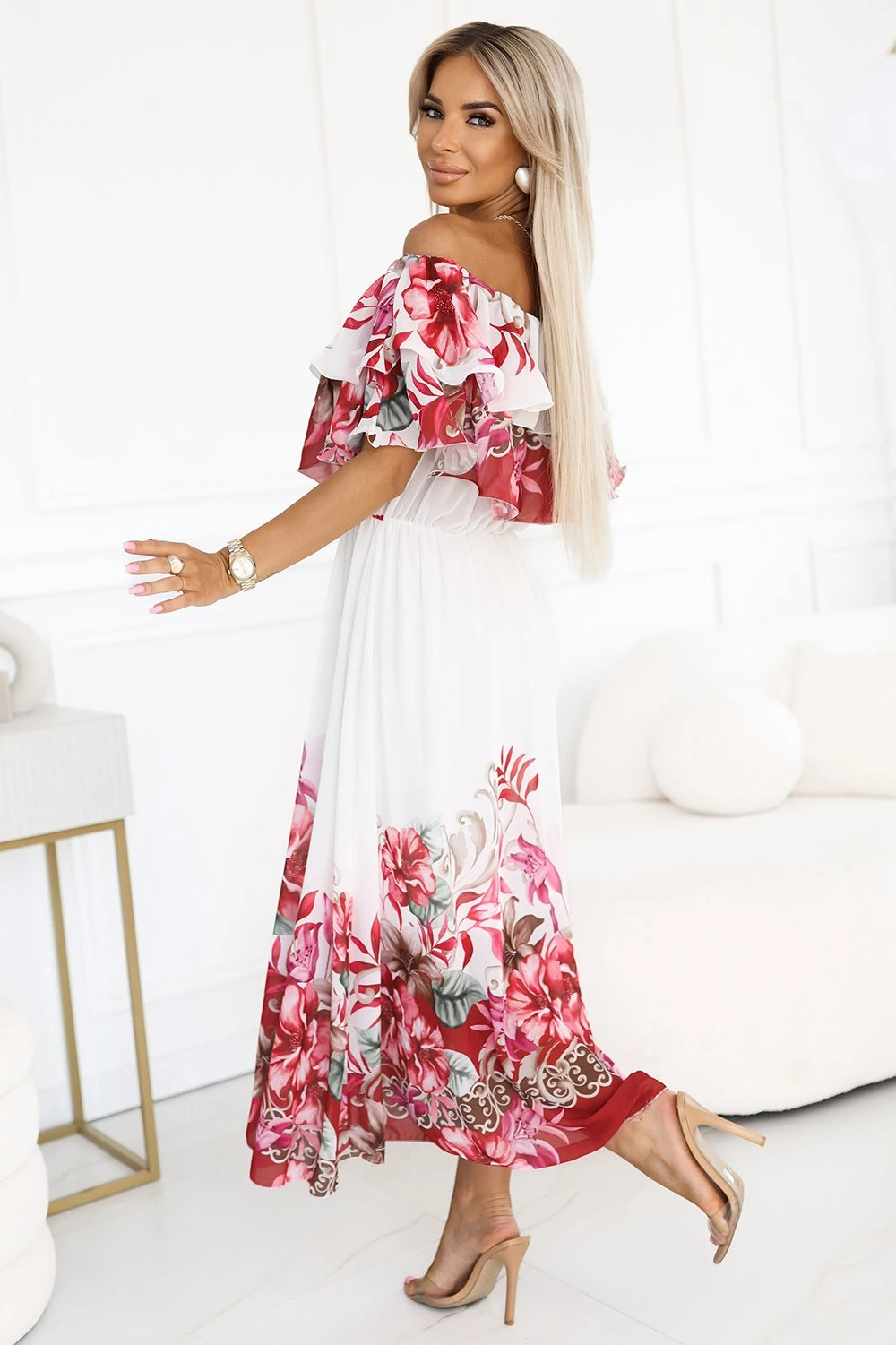 Modelka prezentuje elegancką sukienkę w kwiaty, która zachwyca swoją lekkością i romantycznym stylem. Sukienka w kwiaty idealnie podkreśla kobiecą sylwetkę, dodając jej subtelnego uroku i klasy.
