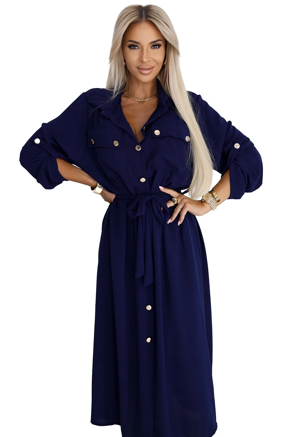 Modelka prezentuje elegancką sukienkę koszulową w głębokim odcieniu granatu, która idealnie podkreśla sylwetkę dzięki wiązaniu w talii. Sukienka koszulowa z ozdobnymi guzikami dodaje stylizacji klasy i nowoczesności.