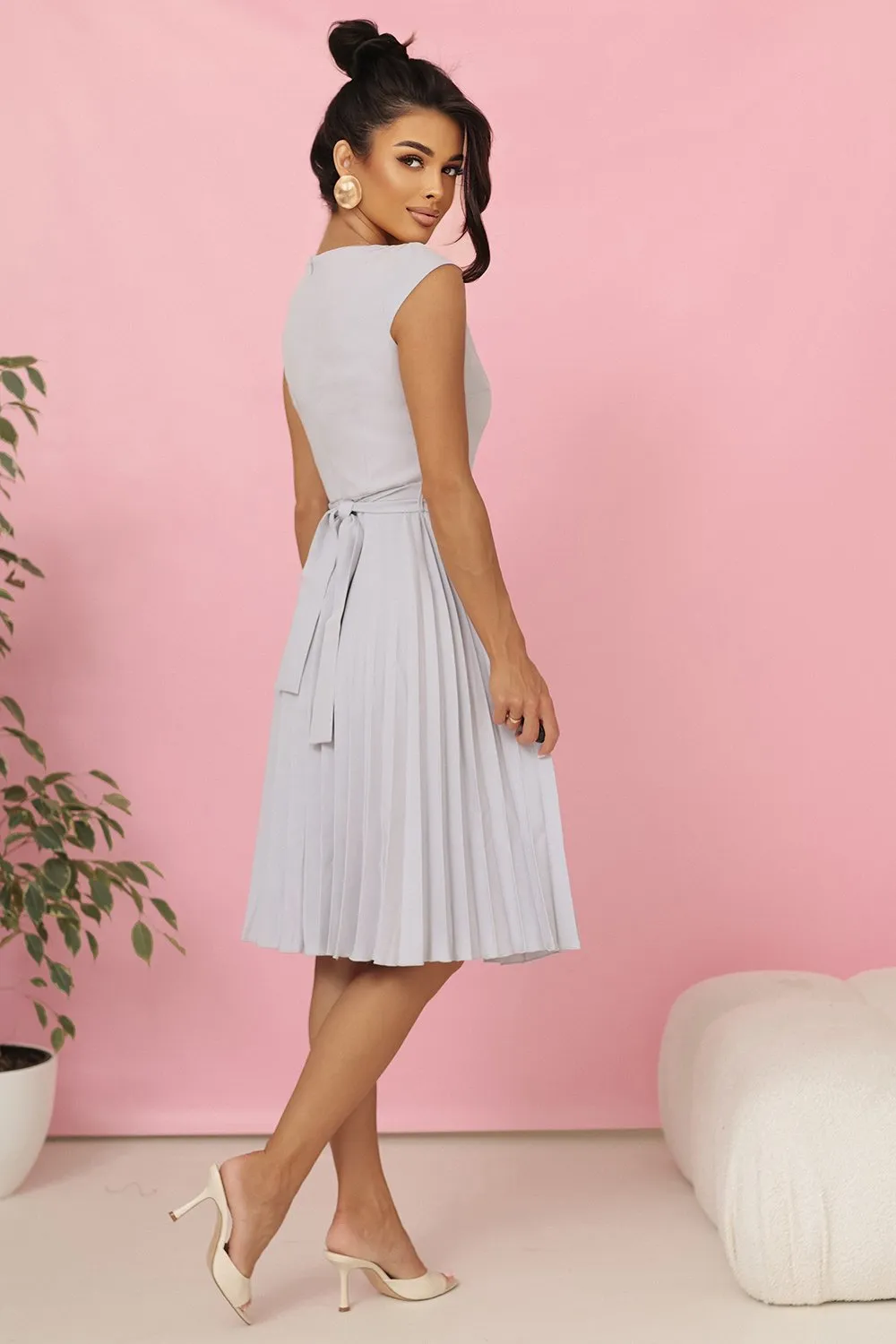 Modelka prezentuje elegancką, plisowaną sukienkę midi, która idealnie podkreśla kobiecą sylwetkę. Sukienka midi z wiązaniem w talii dodaje stylizacji subtelnej klasy i lekkości.