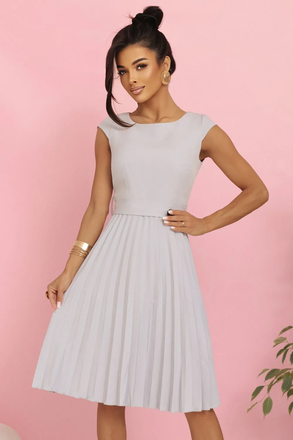 Kobieta na zdjęciu prezentuje elegancką sukienkę midi z plisowanym dołem, która doskonale podkreśla sylwetkę. Ta sukienka midi z plisami to idealny wybór na wyjątkowe okazje, dodając stylu i klasy każdej stylizacji.