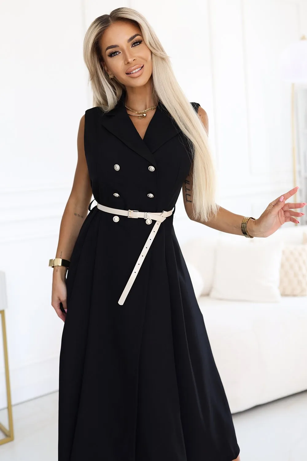 Kobieta na zdjęciu prezentuje elegancką czarną sukienkę z podwójnym rzędem guzików, która idealnie podkreśla jej sylwetkę. Sukienka z paskiem dodaje szyku i klasy, sprawiając, że jest to doskonały wybór na formalne okazje.