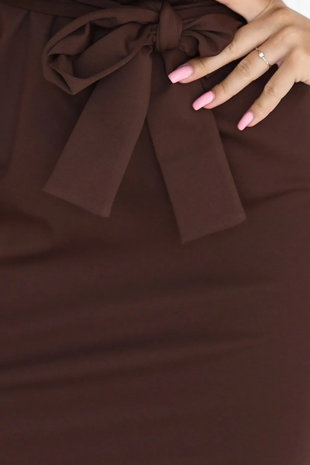 Modelka prezentuje elegancką sukienkę z kokardą w kolorze czekoladowym, która podkreśla talię i dodaje stylizacji wyrafinowanego uroku. Sukienka z kokardą to doskonały wybór na wieczorne wyjścia, łącząc klasykę z nowoczesnym designem.