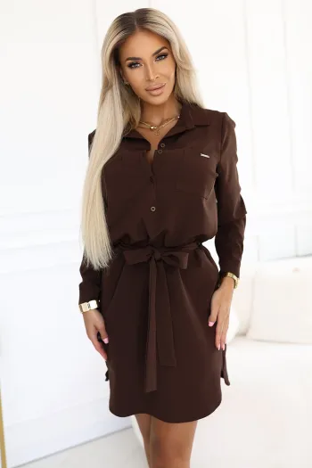 Modelka prezentuje elegancką sukienkę koszulową, która podkreśla sylwetkę dzięki wiązaniu w talii. Ta sukienka koszulowa w głębokim brązowym kolorze doskonale sprawdzi się zarówno na co dzień, jak i na specjalne okazje.
