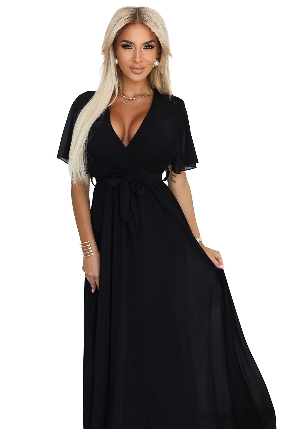 Modelka prezentuje elegancką sukienkę maxi, która zachwyca klasycznym krojem i głębokim dekoltem. Ta czarna sukienka maxi idealnie podkreśla sylwetkę, dodając jej szyku i wyrafinowania.