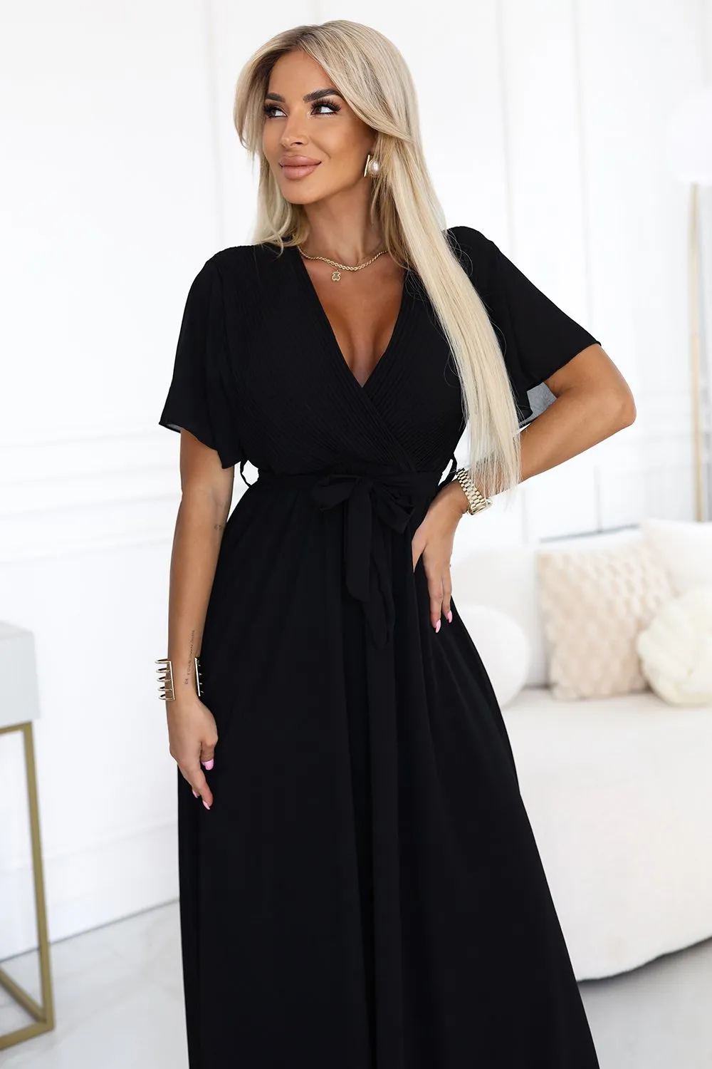 Modelka prezentuje elegancką czarną sukienkę maxi, która podkreśla jej sylwetkę i dodaje klasy. Ta czarna sukienka maxi z wiązaniem w talii to idealny wybór na wieczorne wyjścia.