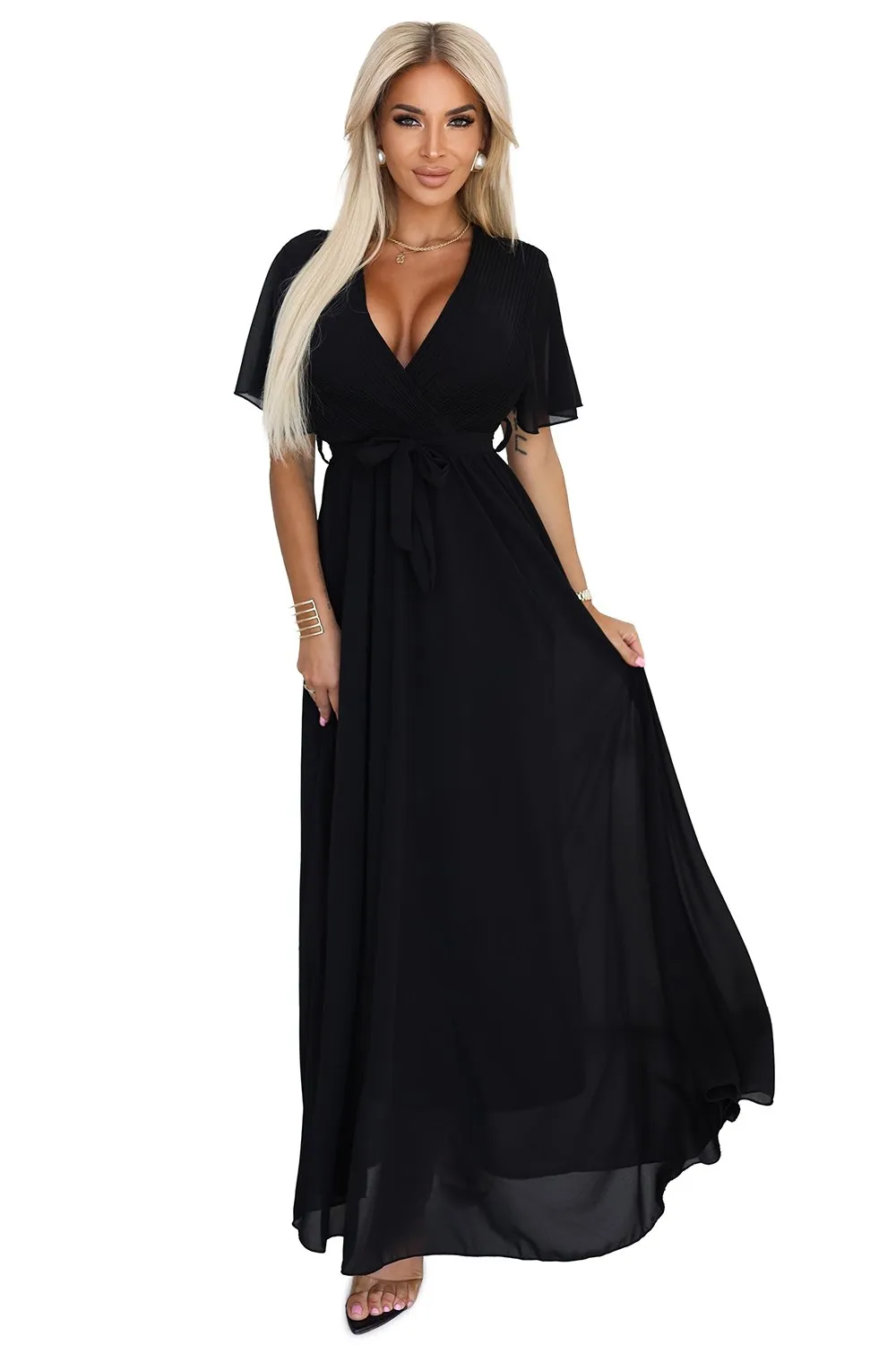 Modelka prezentuje elegancką czarną sukienkę maxi, która doskonale podkreśla sylwetkę i dodaje szyku każdej stylizacji. Sukienka maxi w kolorze czarnym z delikatnym wiązaniem w talii to idealny wybór na wieczorne wyjścia.