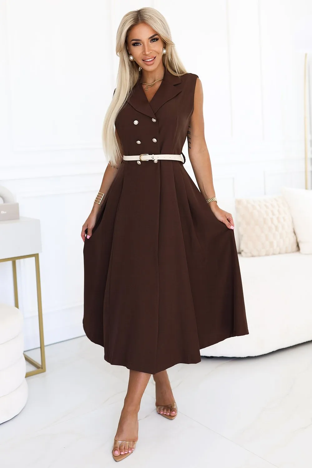 Modelka prezentuje elegancką sukienkę midi w kolorze czekoladowym, która podkreśla sylwetkę dzięki dopasowanemu krojowi i subtelnemu paskowi w talii. Ta stylowa sukienka midi z dwurzędowym zapięciem idealnie sprawdzi się na formalne okazje, dodając klasy i szyku każdej stylizacji.