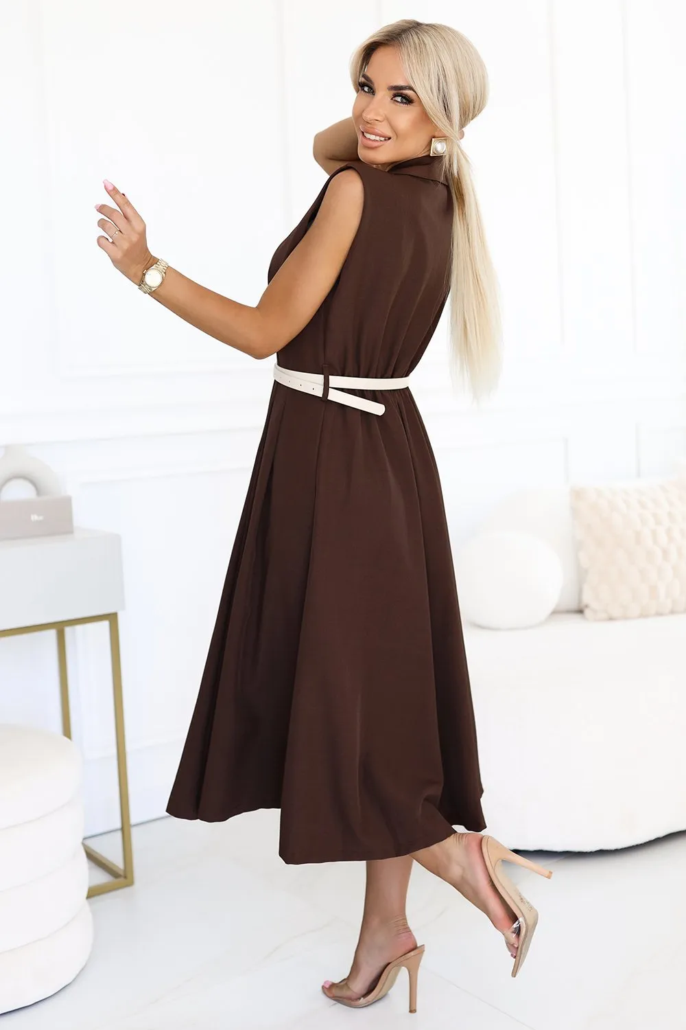 Kobieta na zdjęciu prezentuje elegancką sukienkę midi w kolorze czekoladowym, która idealnie podkreśla jej sylwetkę. Sukienka midi jest zestawiona z delikatnym, jasnym paskiem, dodającym całości subtelnego kontrastu.