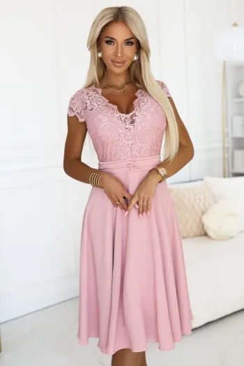 Kobieta na zdjęciu prezentuje elegancką sukienkę koronkową w odcieniu pudrowego różu, która idealnie podkreśla jej sylwetkę. Sukienka koronkowa z delikatnym wzorem i rozkloszowanym dołem dodaje stylizacji lekkości i romantyzmu.