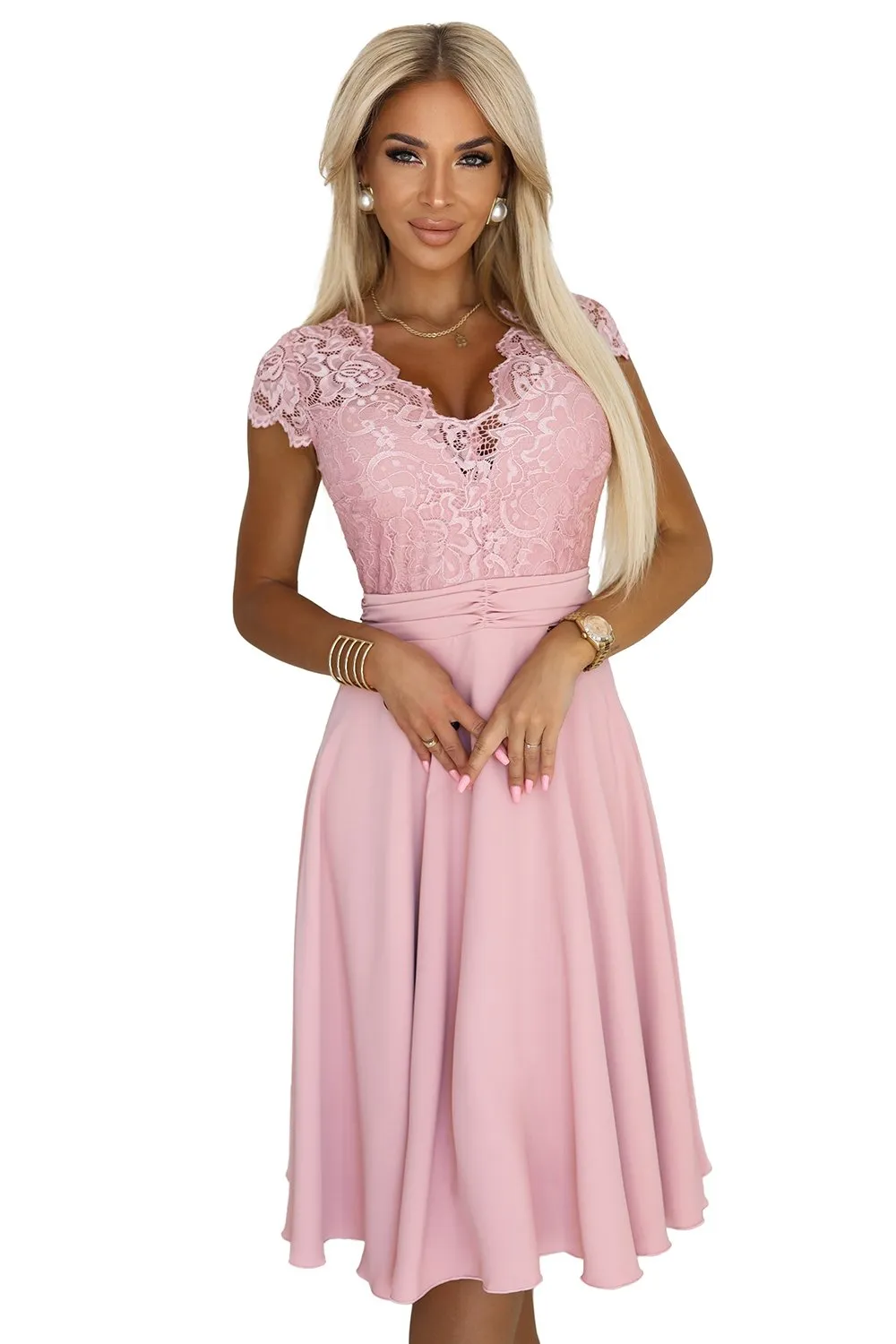 Modelka prezentuje elegancką sukienkę koronkową, która łączy w sobie delikatność materiału z klasycznym krojem. Ta różowa sukienka koronkowa idealnie podkreśla sylwetkę, dodając subtelnego uroku i kobiecości.