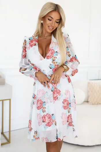 Kobieta na zdjęciu prezentuje elegancką sukienkę w kwiaty, która idealnie podkreśla jej sylwetkę. Sukienka w kwiaty wyróżnia się delikatnym wzorem i subtelną kolorystyką, dodając stylizacji lekkości i kobiecości.