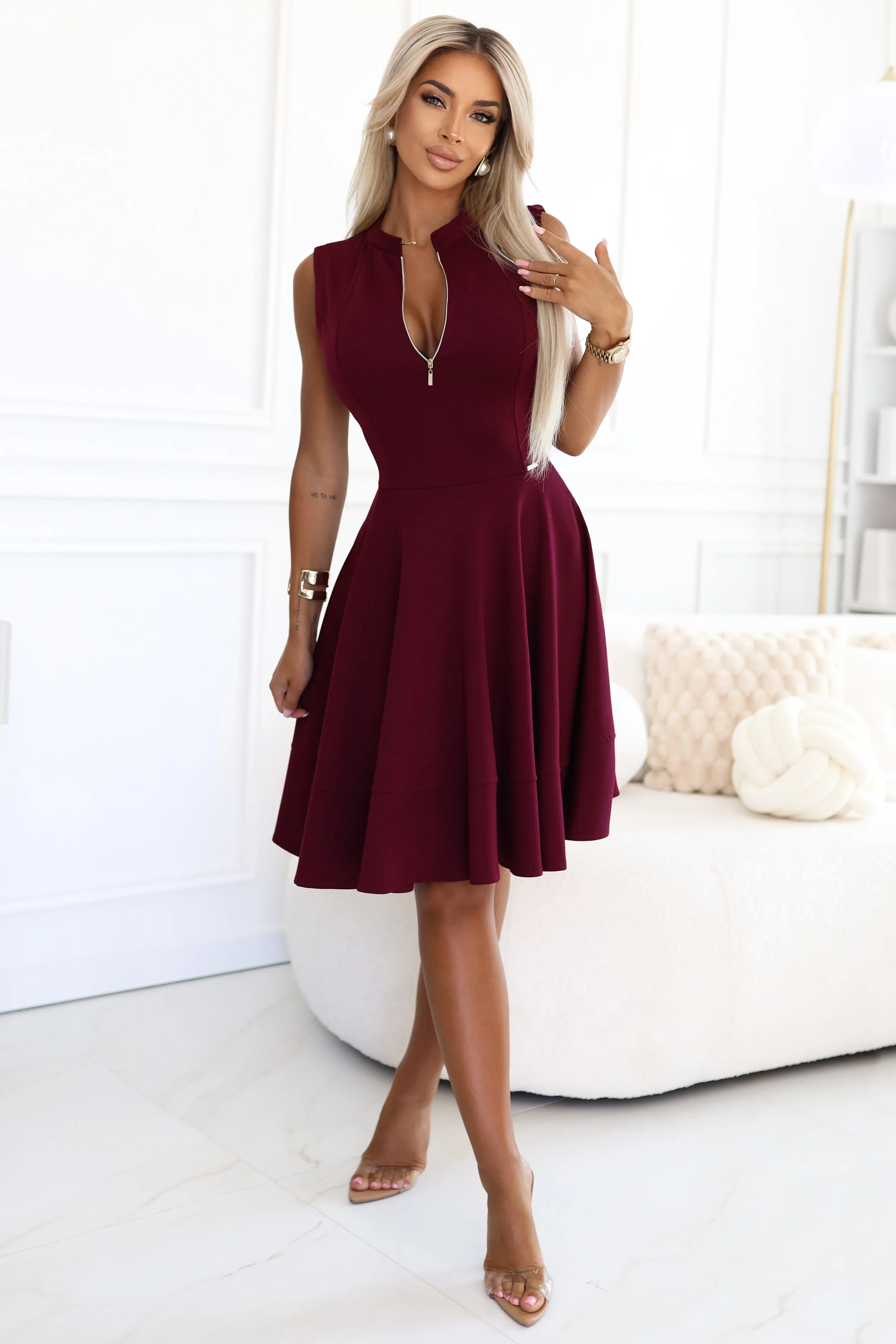 Modelka prezentuje elegancką sukienkę bordową, która idealnie podkreśla sylwetkę i dodaje szyku każdej stylizacji. Sukienka bordowa z zamkiem na dekolcie to doskonały wybór na wieczorne wyjścia i specjalne okazje.