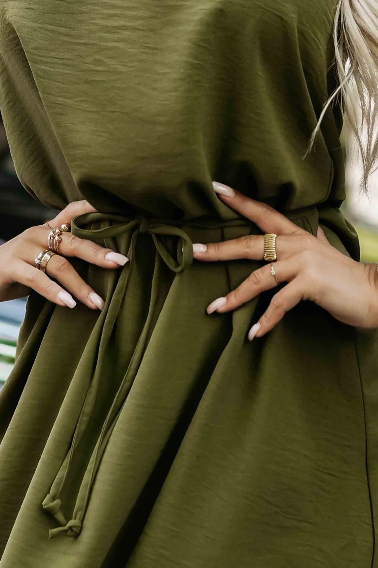 Modelka prezentuje elegancką sukienkę w kolorze oliwkowym, która idealnie podkreśla sylwetkę dzięki wiązaniu w talii. Ta oliwkowa sukienka to doskonały wybór na każdą okazję, łącząc styl z komfortem.