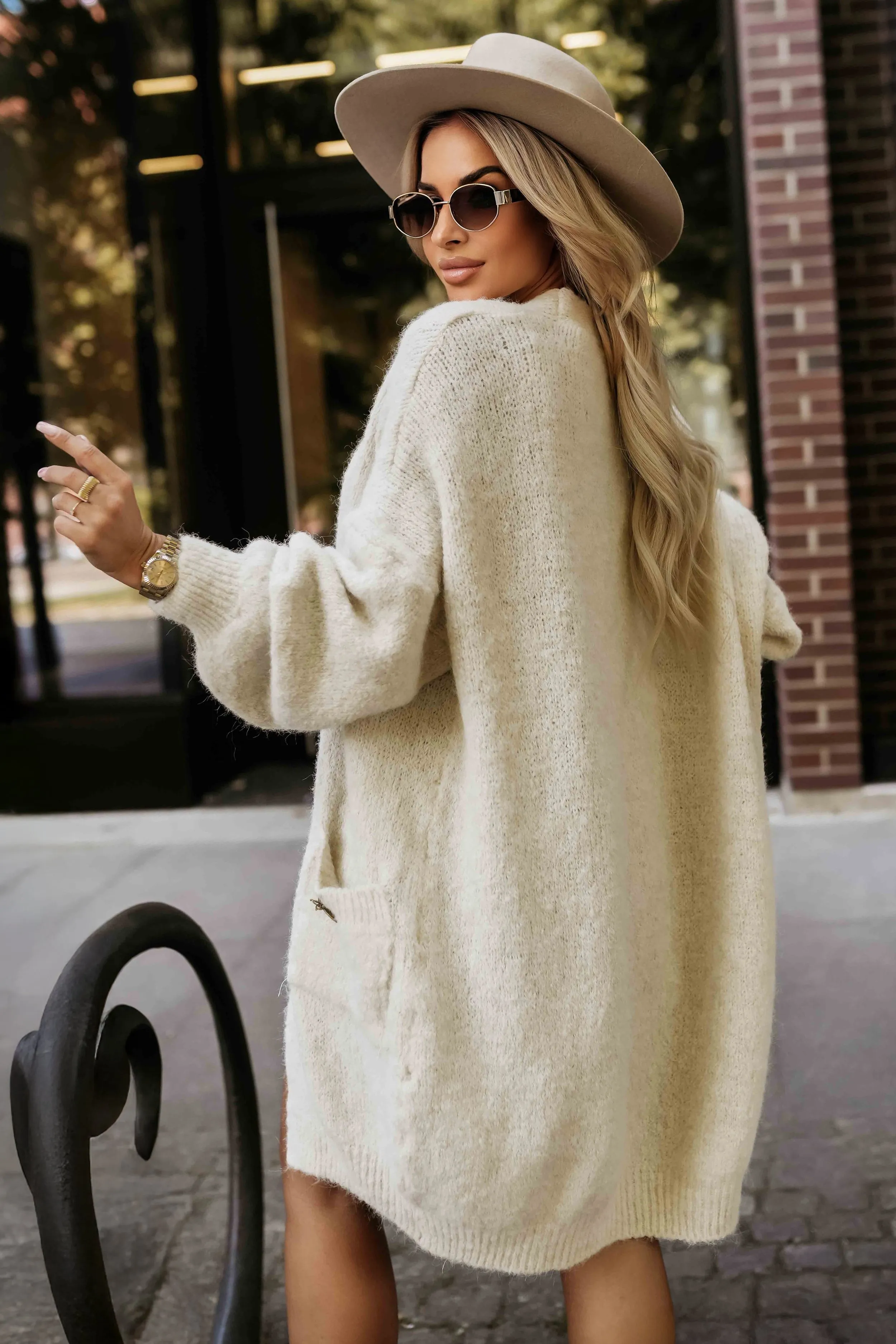 Kobieta na zdjęciu prezentuje elegancki, kremowy sweter oversize, który idealnie wpisuje się w miejską modę. Sweter oversize dodaje stylizacji lekkości i jest doskonałym wyborem na chłodniejsze dni.