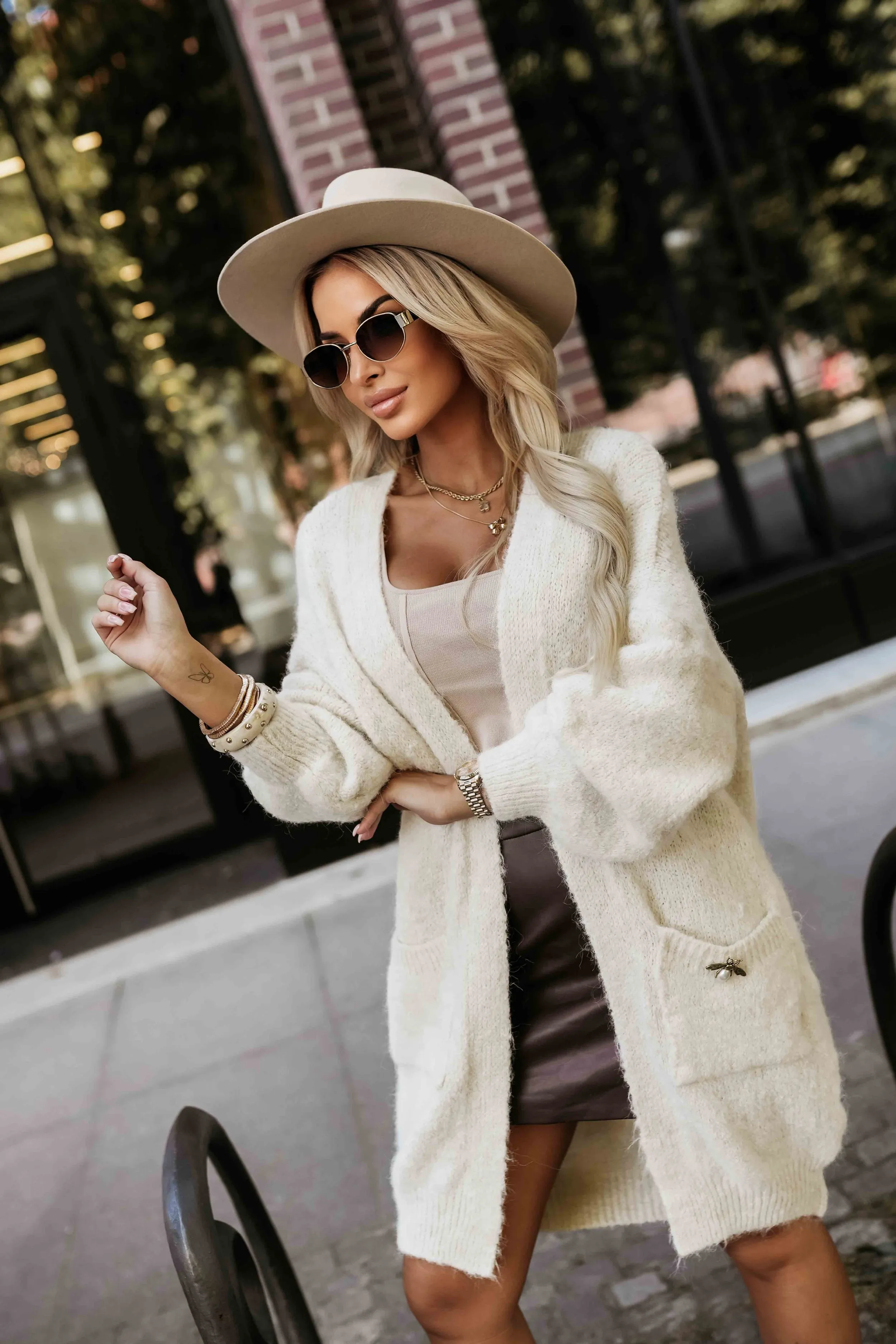Modelka prezentuje elegancki, kremowy kardigan z miękkiej dzianiny, który idealnie komponuje się z casualowym stylem. Kardigan z kieszeniami i ozdobnym detalem dodaje szyku i jest doskonałym wyborem na chłodniejsze dni.