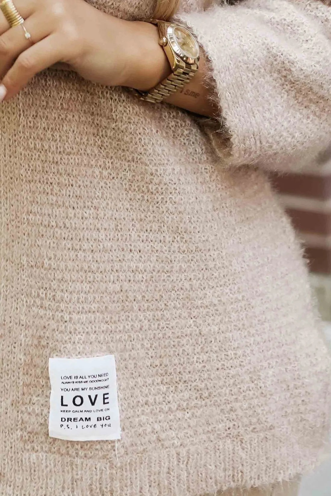 Modelka prezentuje elegancki, beżowy sweter Love, który wyróżnia się miękką fakturą i subtelnym designem. Ten sweter Love idealnie łączy styl z komfortem, dodając ciepła każdej stylizacji.