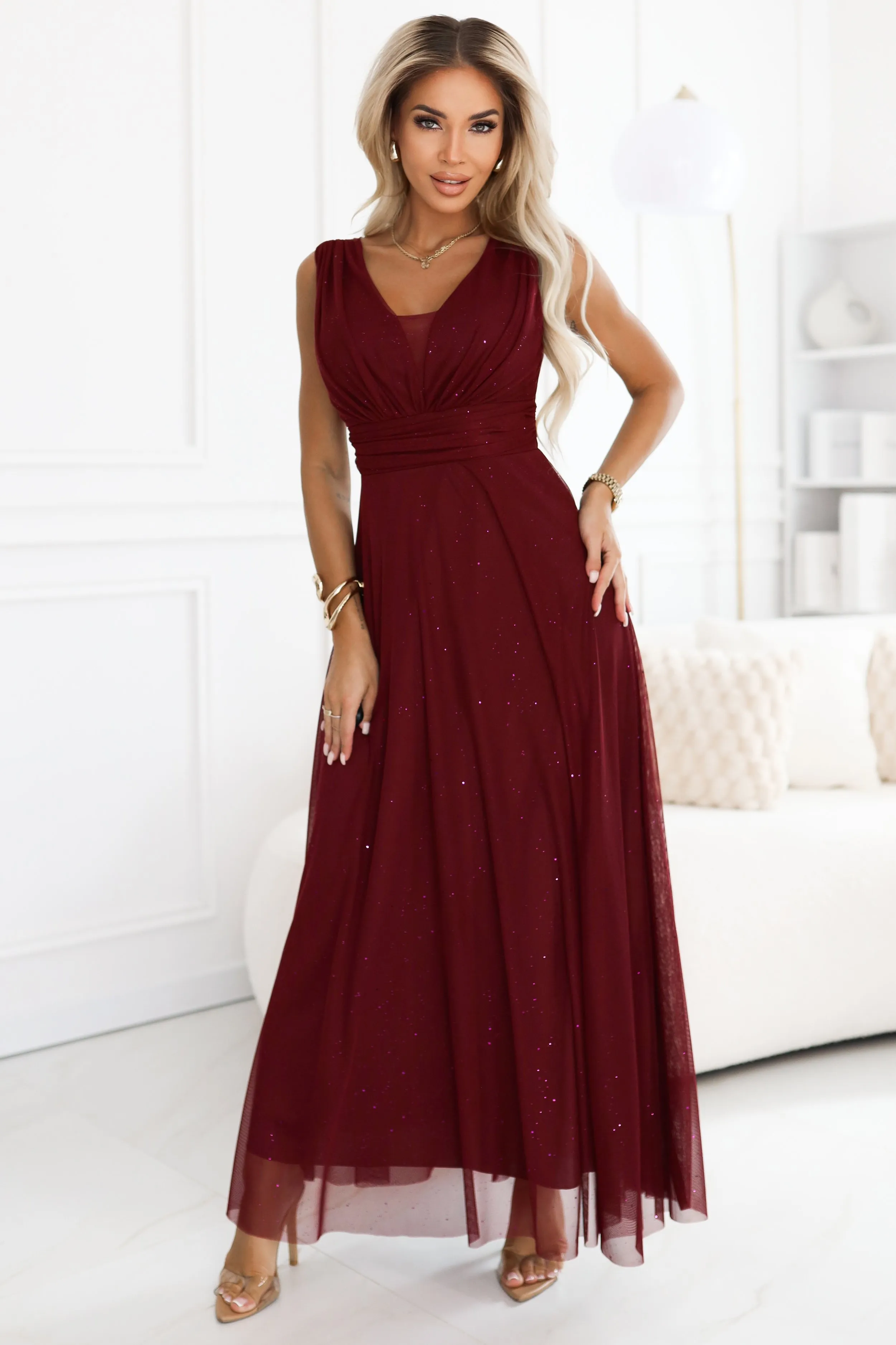 Modelka prezentuje elegancką suknię wieczorową o głębokim burgundowym kolorze. Suknia wieczorowa zachwyca delikatnym połyskiem i klasycznym krojem, idealnym na wyjątkowe okazje.